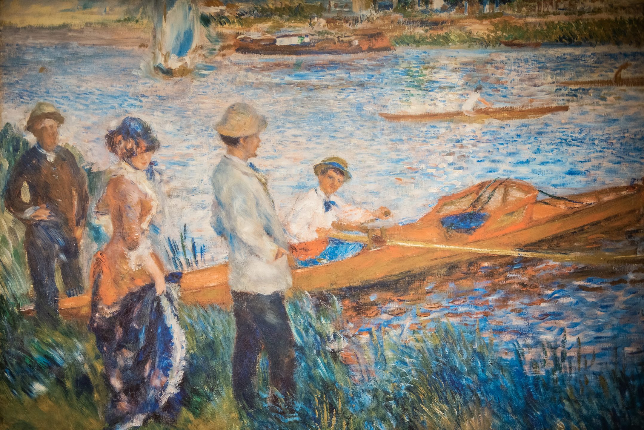 An impressionist painting depicts two men and a woman standing by a riverside, watching another man sitting in a yellow rowboat on the water. Additional boats and greenery are visible in the background.